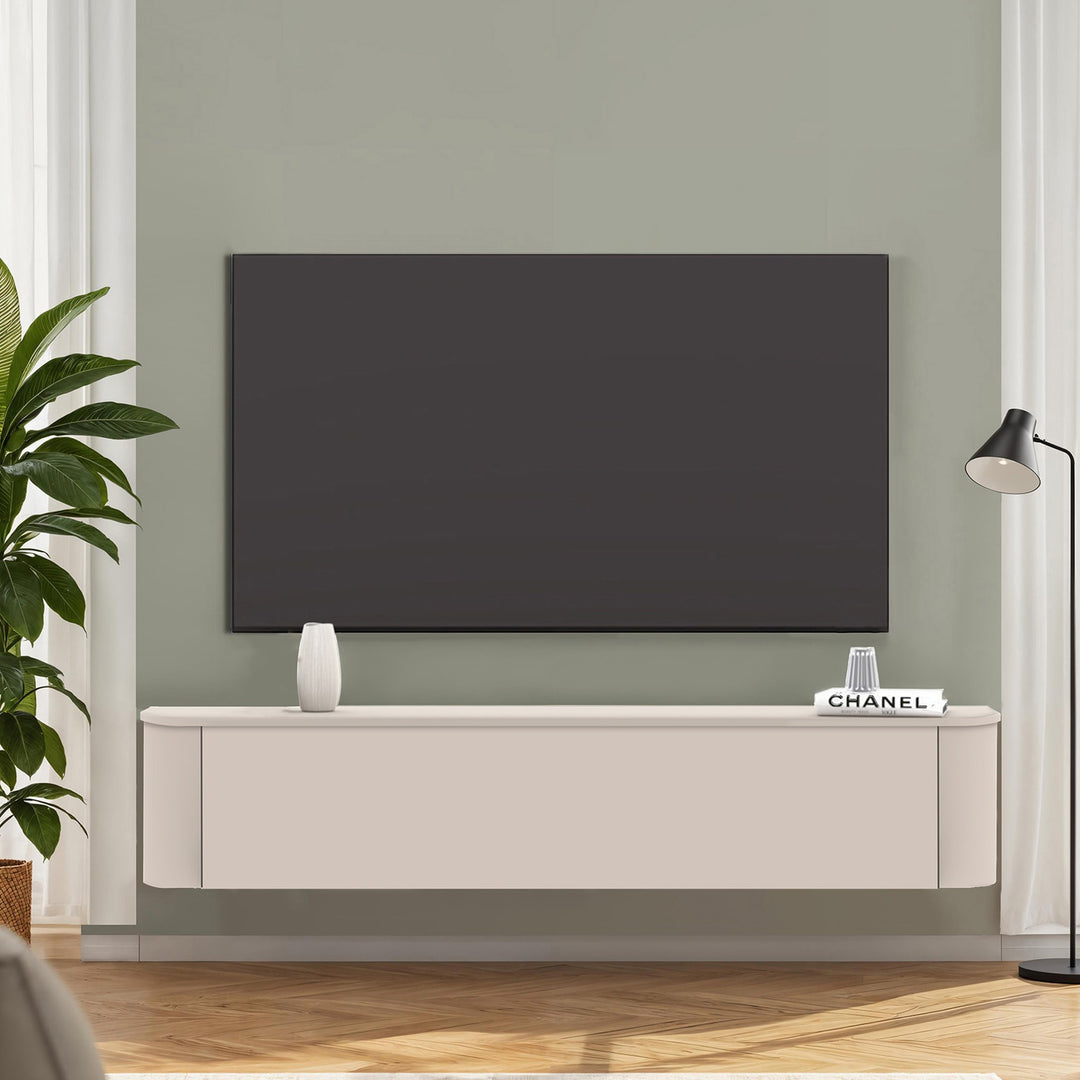 Lido TV-benk i kremhvit, veggmontert under TV mot salviegrønn vegg med plante og gulvlampe.