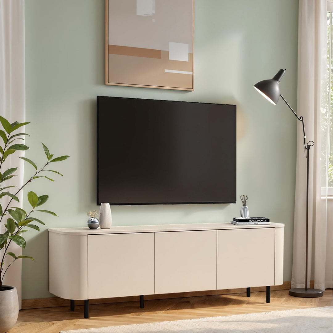 Lido TV-benk i kremhvit på sorte ben mot salviegrønn vegg med TV, plante og gulvlampe.