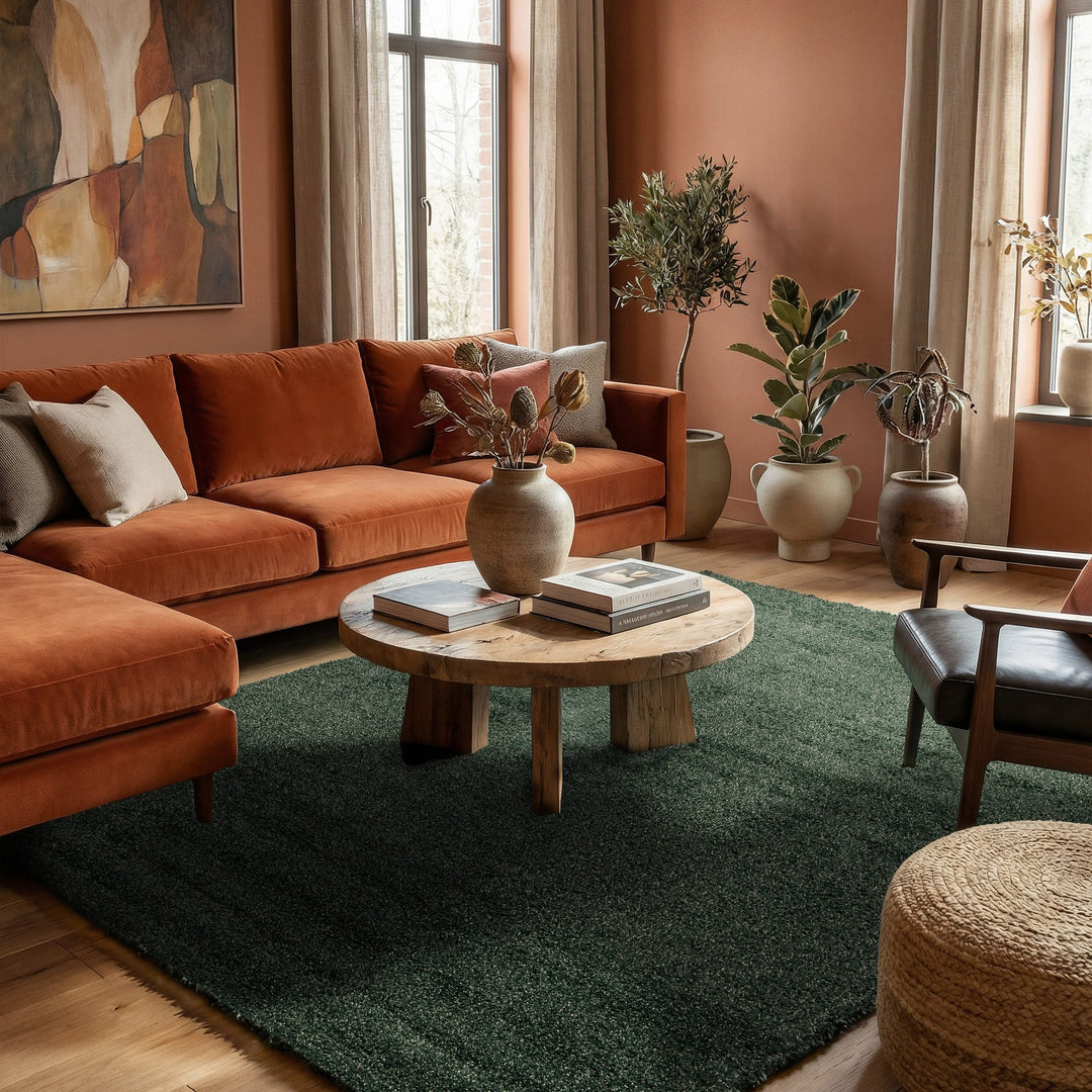Lone Amea teppe i mørk grønn på tregulv foran rustfarget sofa med planter og rundt sofabord