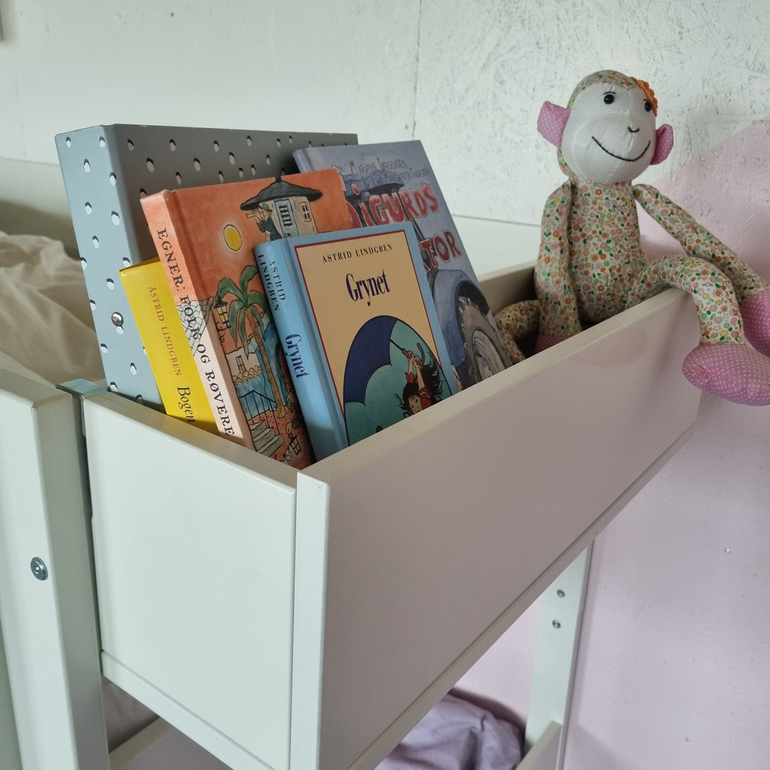 Manis-h Huxie bokkasse i hvitt montert på seng med bøker og apekatt-bamse