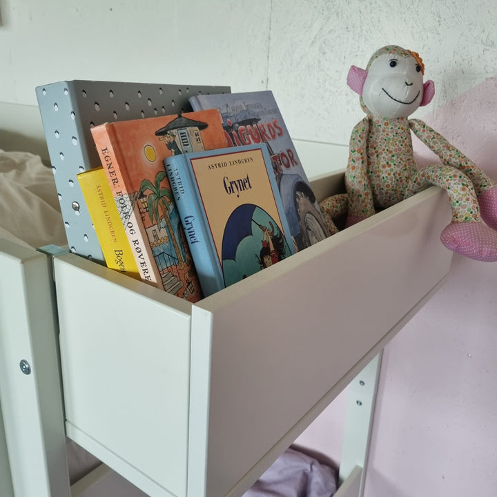 Manis-h Huxie bokkasse i hvitt montert på seng med bøker og apekatt-bamse