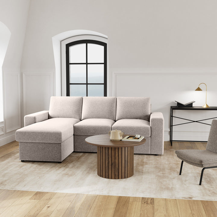 Conan sovesofa i lys beige med sjeselong, rundt trebord og buevindu i lyst rom