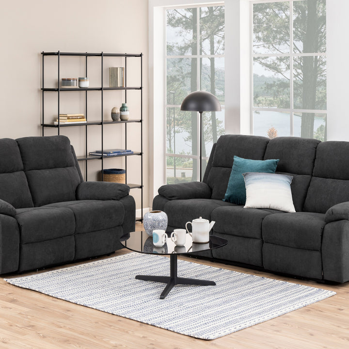 Mora reclinersofa i mørk grå stoff i stue med sort gulvlampe og utsikt mot vann