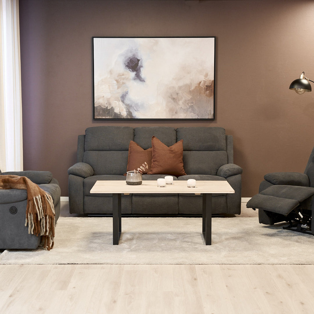 Mora reclinersofa i mørk grå i brun stue med sofabord og veggbilde.