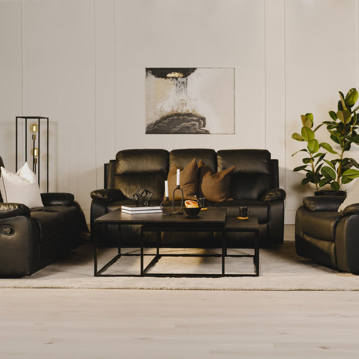 Mora reclinersofa i sort kunstskinn med lenestoler i lys stue med mørkt sofabord og plante