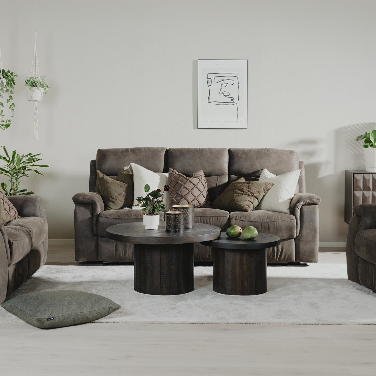 Mayfield sofa i brunt stoff i lys stue med runde mørke trebord, grønne planter og veggplakat