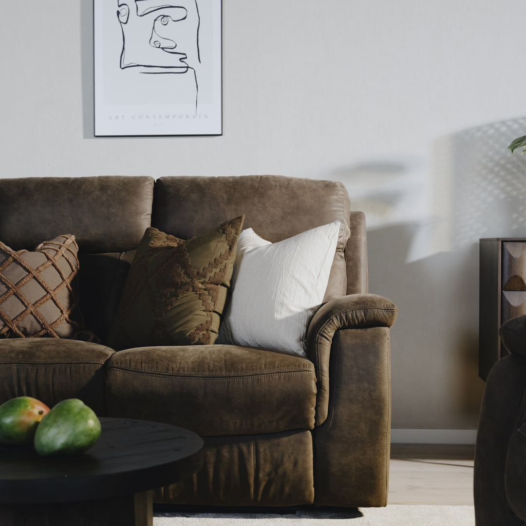 Mayfield sofa i gråbrunt stoff med pynteputer, mørkt rundbord og veggkunst i stuemiljø