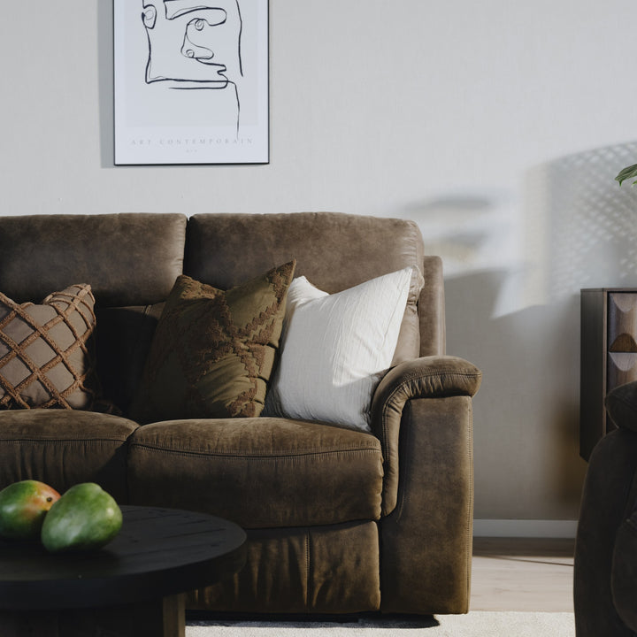 Mayfield sofa i gråbrunt stoff med pynteputer, mørkt rundbord og veggkunst i stuemiljø