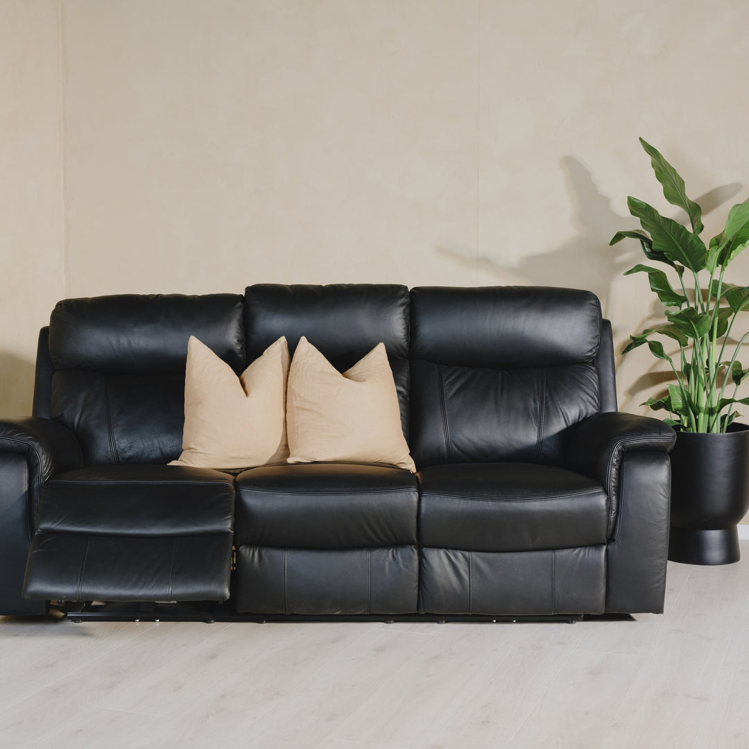 Mayfield sofa i sort skinn, 3-seter med beige puter og grønn plante i stuemiljø