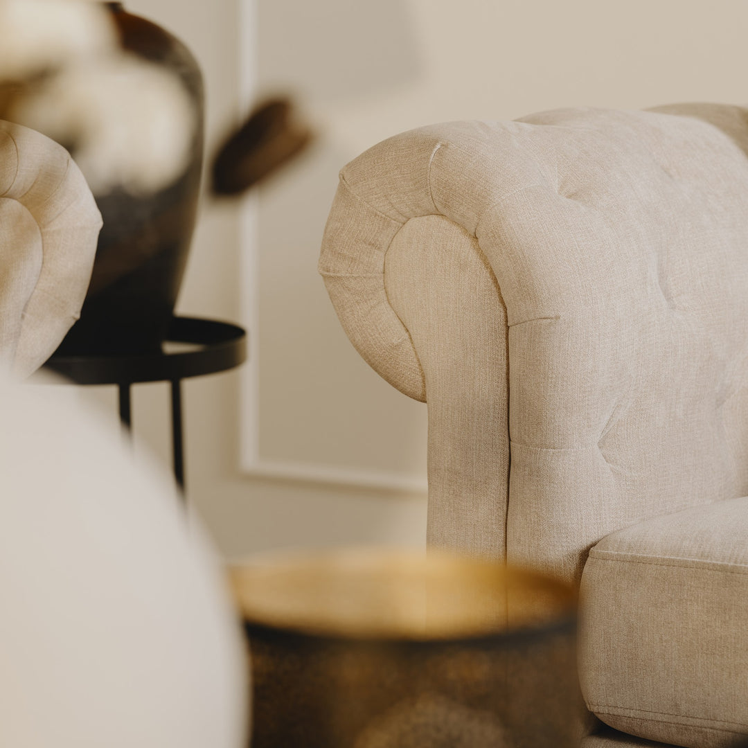 Charlietown sofa, stemningsbilde av tuftet, beige armlene med sidebord og vase.