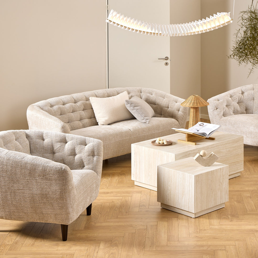 Ria sofa i lys beige stoff med knappet rygg, matchende lenestol og lyse travertinbord