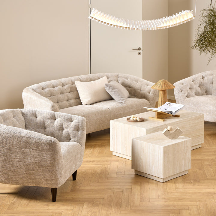 Ria sofa i lys beige stoff med knappet rygg, matchende lenestol og lyse travertinbord
