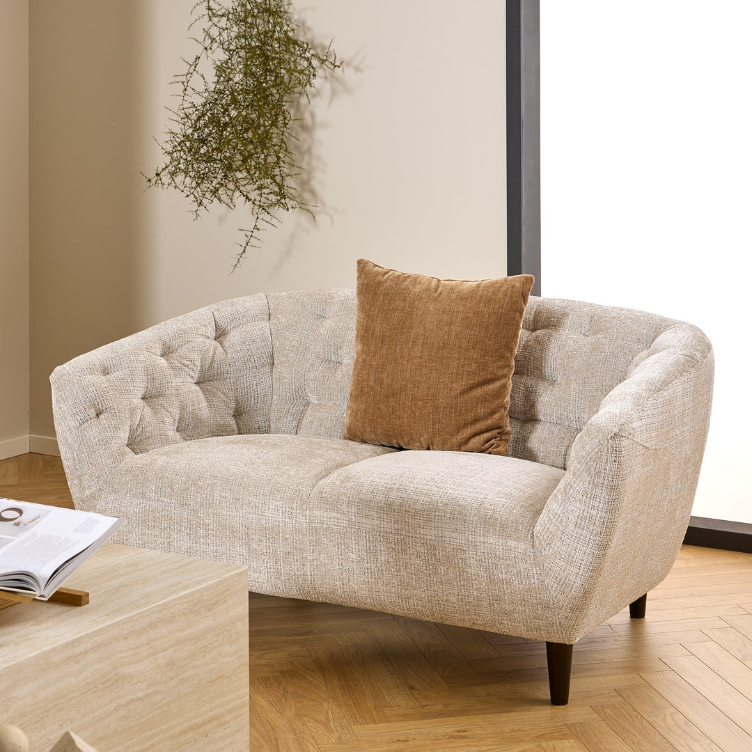 Ria 2-seter i beige chenille med brun pute i stue, hengeplante og parkettgulv.