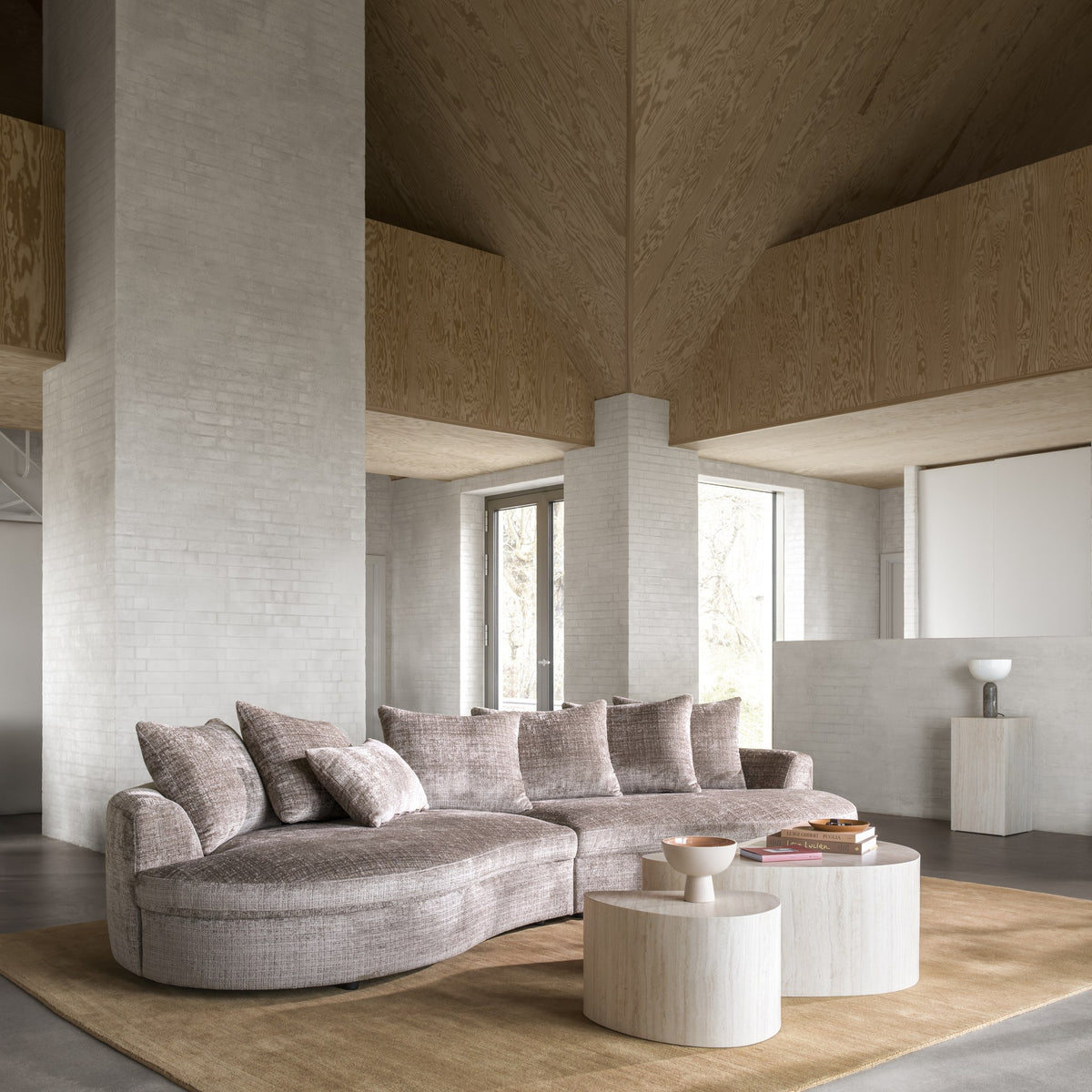 Cordova sofa i gråbrunt stoff med buet sjeselong i lyst loftsrom med teglvegg og runde bord