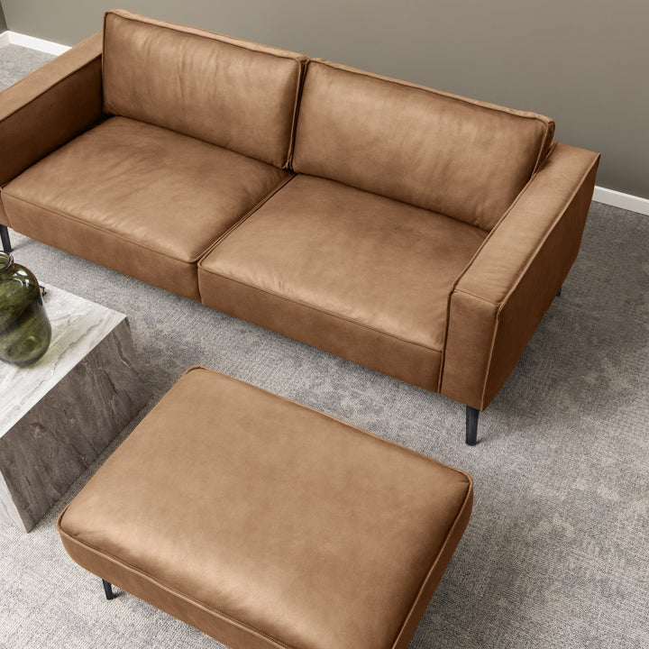 Montebello sofa i cognac skinn med matchende puff, sett ovenfra i stue med grått teppe