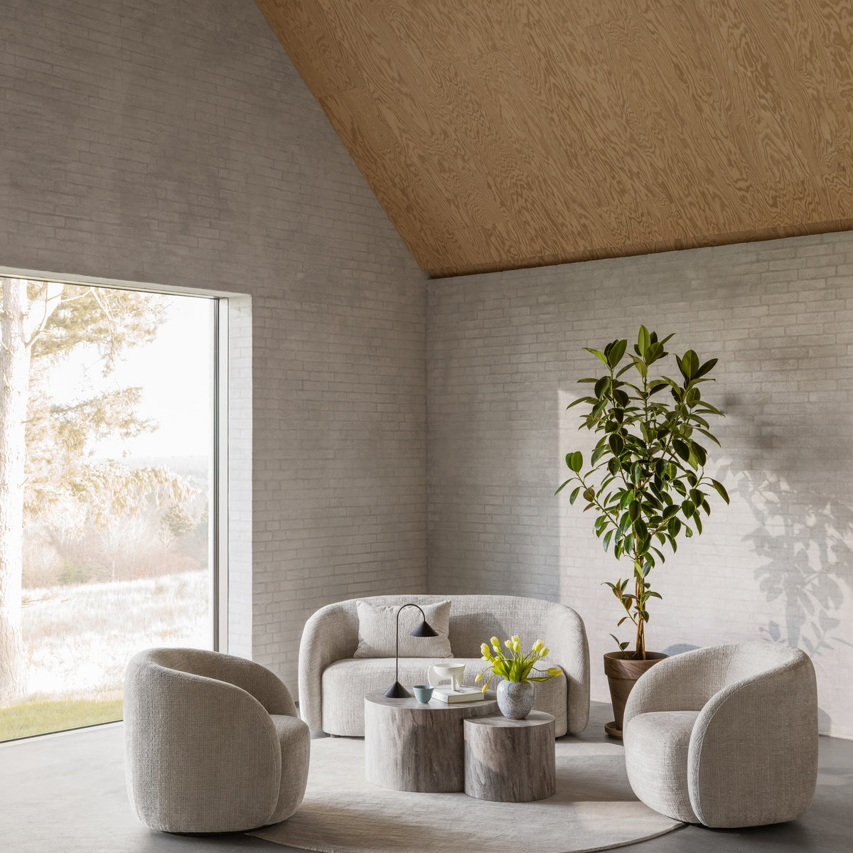 Lodi sofa i lys bouclé med runde lenestoler i lyst rom med teglvegg, grønn plante og trebord
