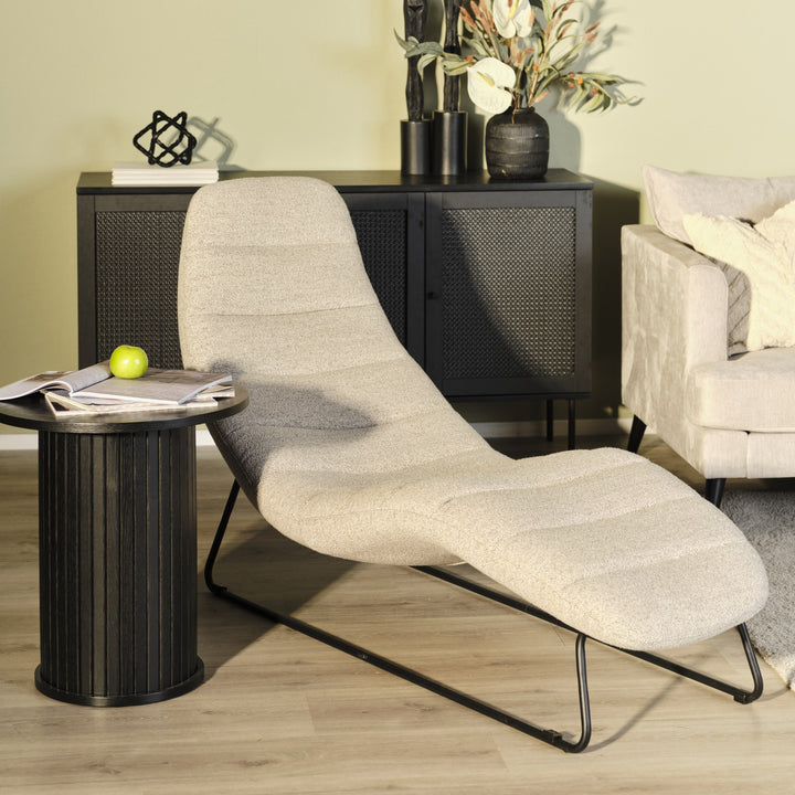 Chaplin loungestol i sandfarget bouclé ved sort sidebord, rottingskjenk og beige sofa