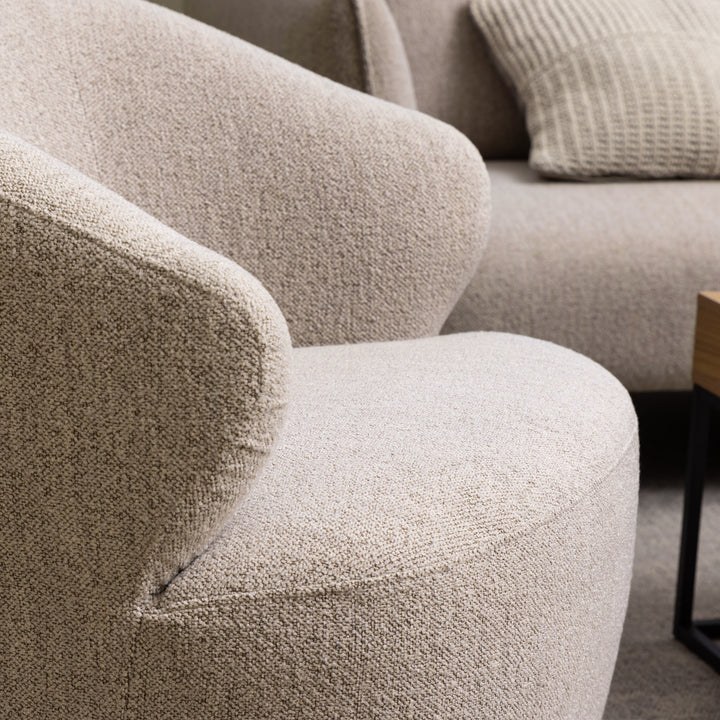 Westport loungestol i lys beige bouclé, nærbilde av armlene med pute og sofa bak
