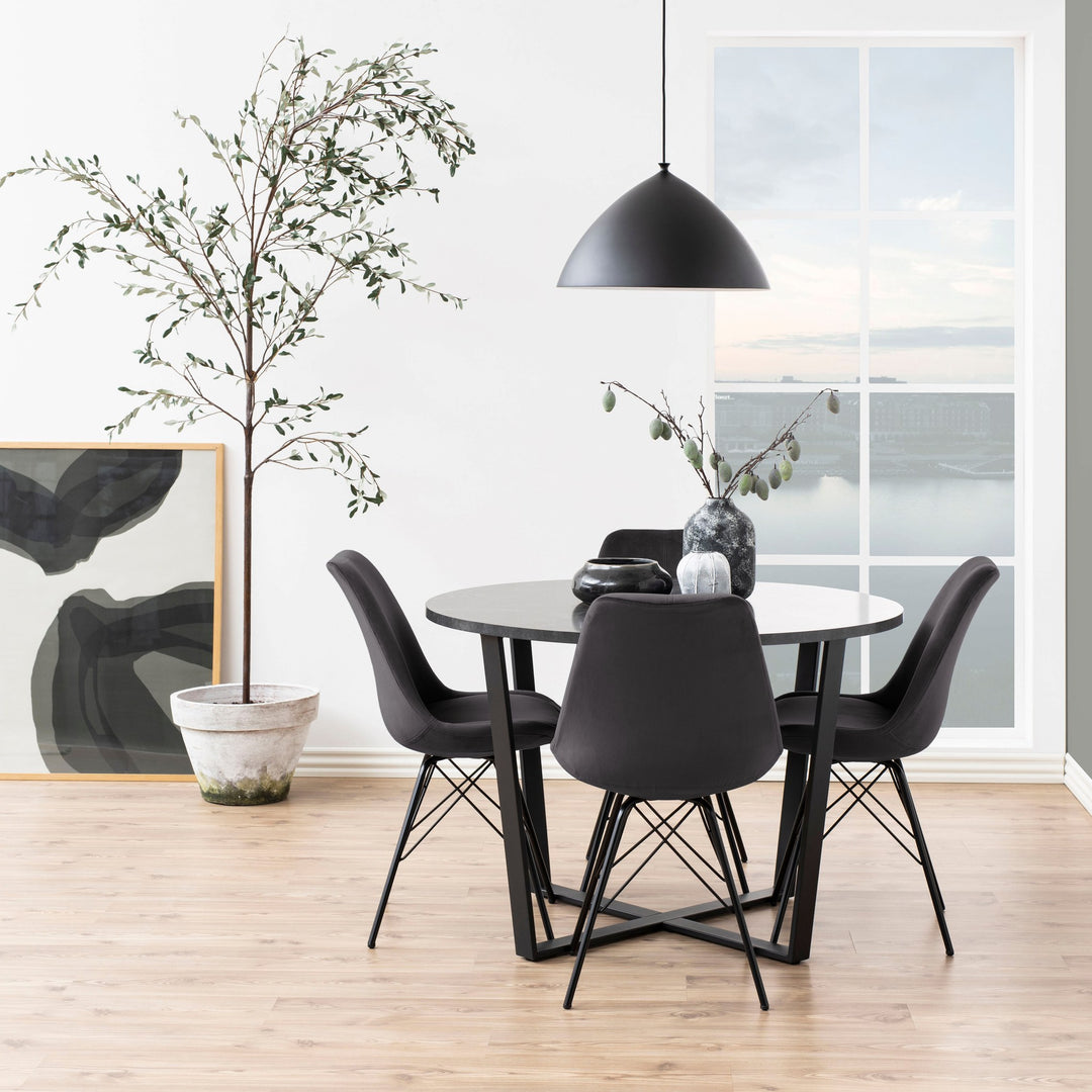 Amble spisebord med rund plate i sort marmorlook, sorte skallstoler, taklampe og oliventre.