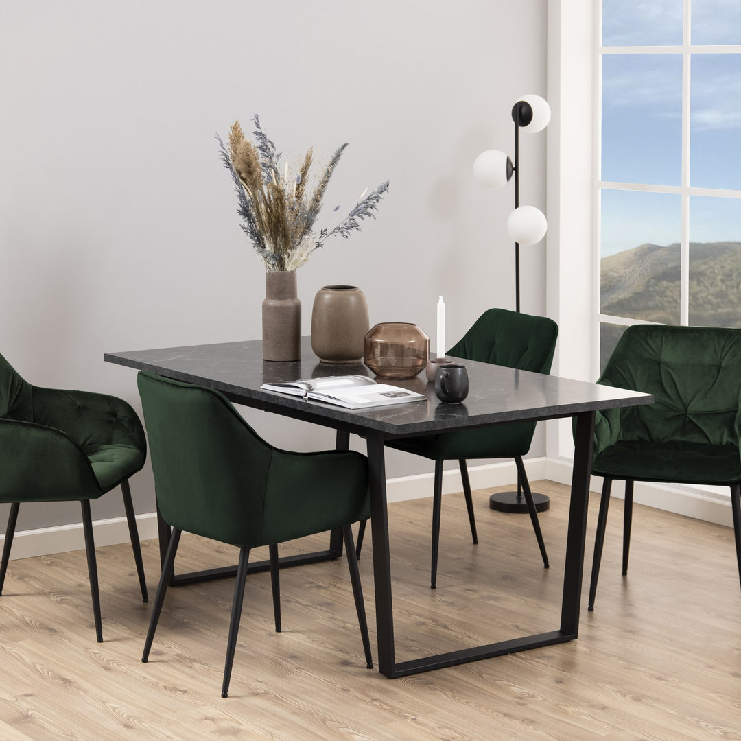 Amble spisebord med rektangulær plate i sort marmorlook, grønne velourstoler og gulvlampe.