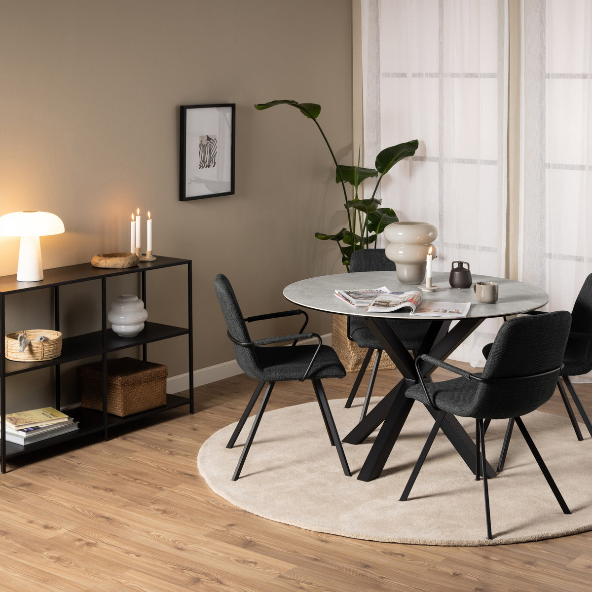 Earth spisebord, rundt med grå steinplate og svart kryssben, omgitt av mørkegrå stoler på beige teppe med grønn plante
