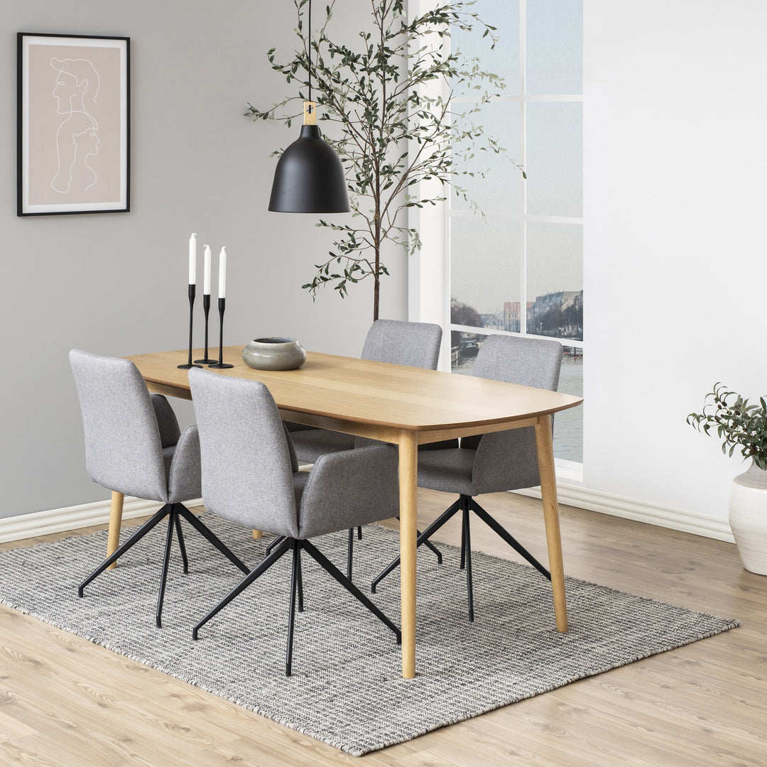 Naya spisestol i lys grå, vist rundt lyst eikebord i spisestue med oliventre og vindu