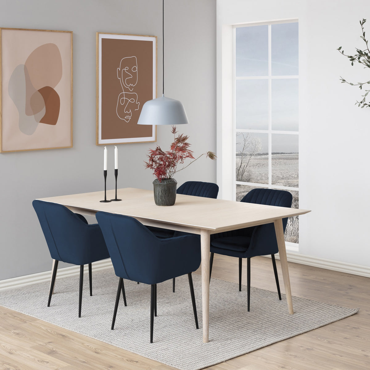 Emilia spisestol i marineblå velur med svarte ben, ved lyst trebord med pendel og veggkunst