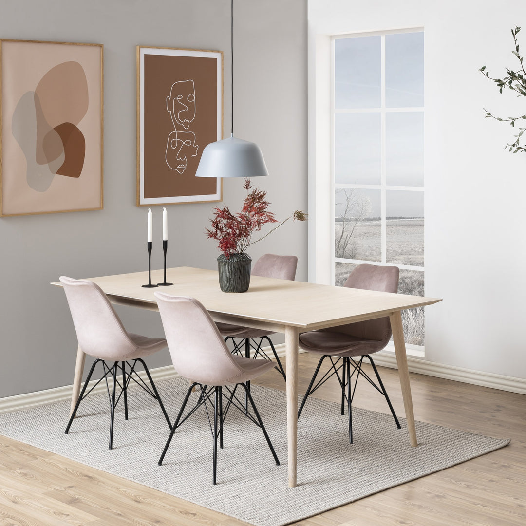 Eris spisestol i støvet rosa velur med sorte ben, rundt lyst spisebord i stue med kunst på veggen
