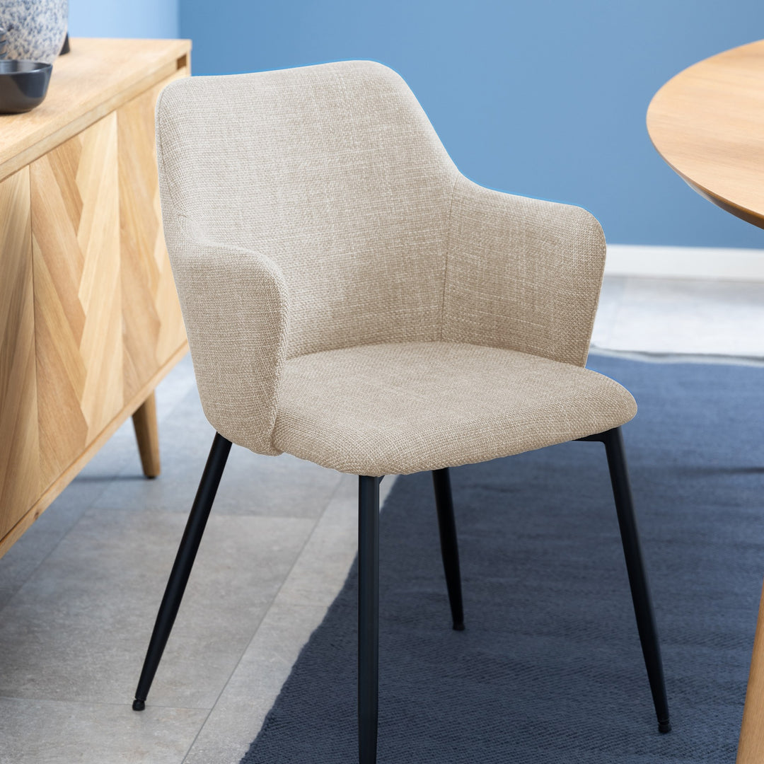 Ilsa spisestol i beige tekstil med armlener og svarte ben ved eikeskjenk i lyst rom