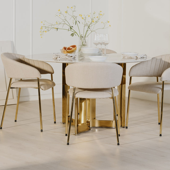 Ann spisestoler i beige stoff med gullben rundt hvitt bord med gullfot, dekket med blomster og glass