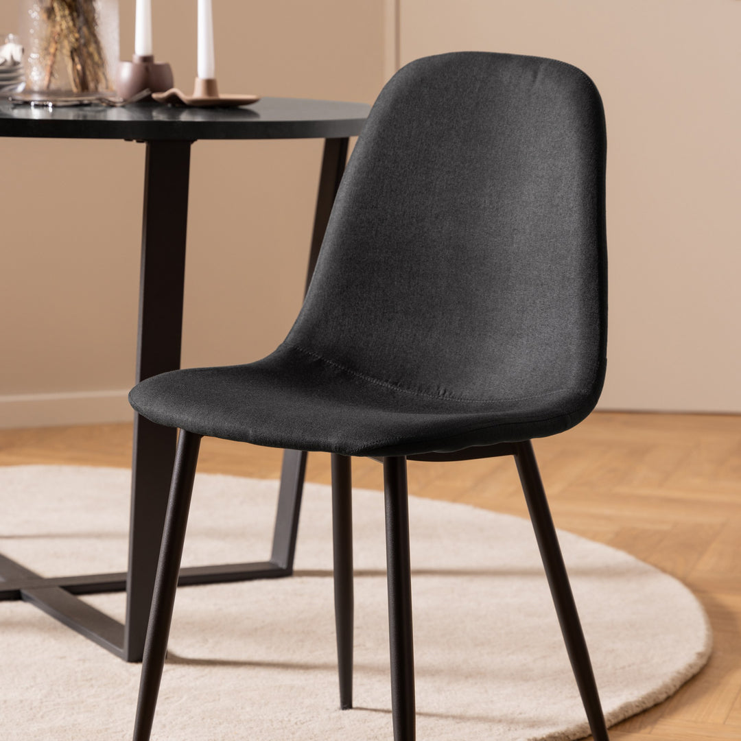 Celia spisestol i sort stoff med svarte ben, ved sort rundt spisebord på beige teppe