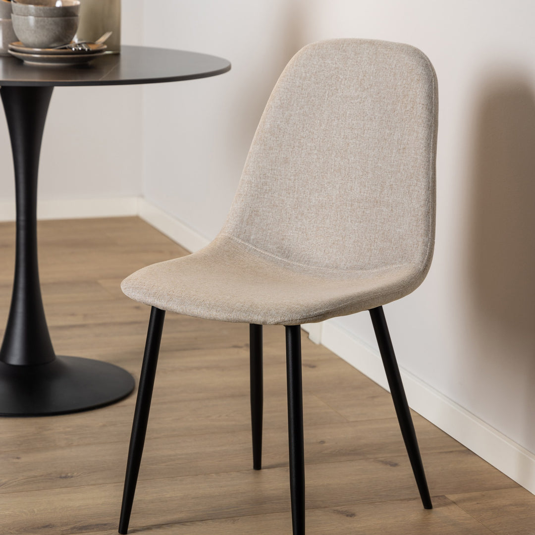 Celia spisestol i beige stoff med svarte ben, ved sort rundt spisebord på lyst tregulv