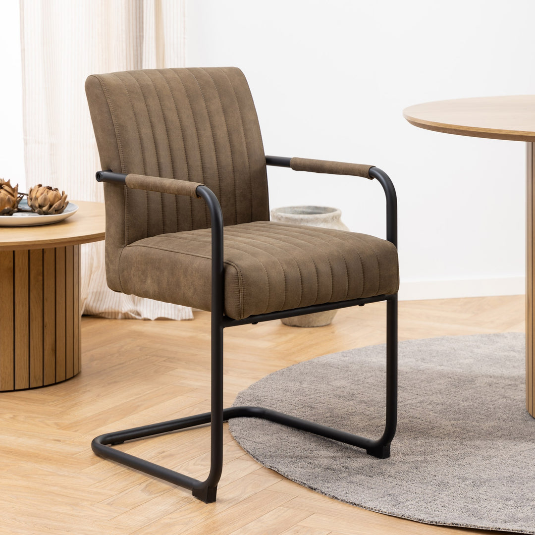 Ellen spisestol i lys brun stoff med sorte armlener og meder, foran gardin med plante i krukke