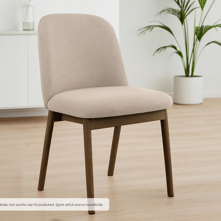 Leo spisestol i beige stoff med brune treben, foran hvit kommode med grønn plante