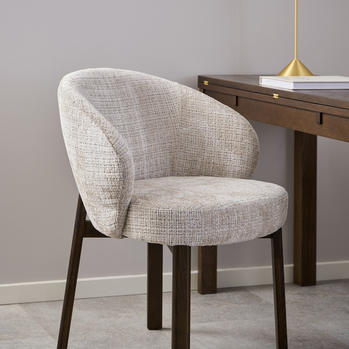 Darlene spisestol i lys gråmelert stoff med mørke treben, ved skrivebord med messinglampe