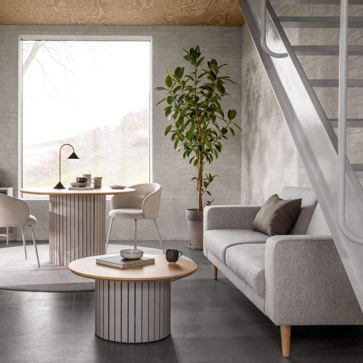 Eleanor spisestol i beige stoff ved rundt eikebord, i stue med grå sofa, plante og trapp.