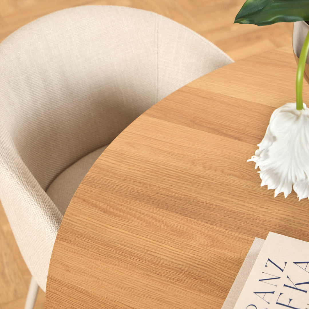 Eleanor spisestol i beige stoff ved rundt eikebord med hvit blomst og bok.