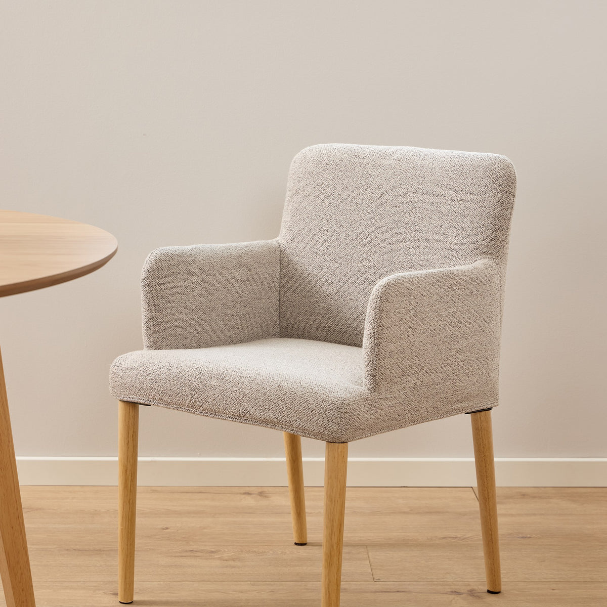 Zoe spisestol i lys beige bouclé med eikeben, ved lyst rundt spisebord på fiskebensparkett