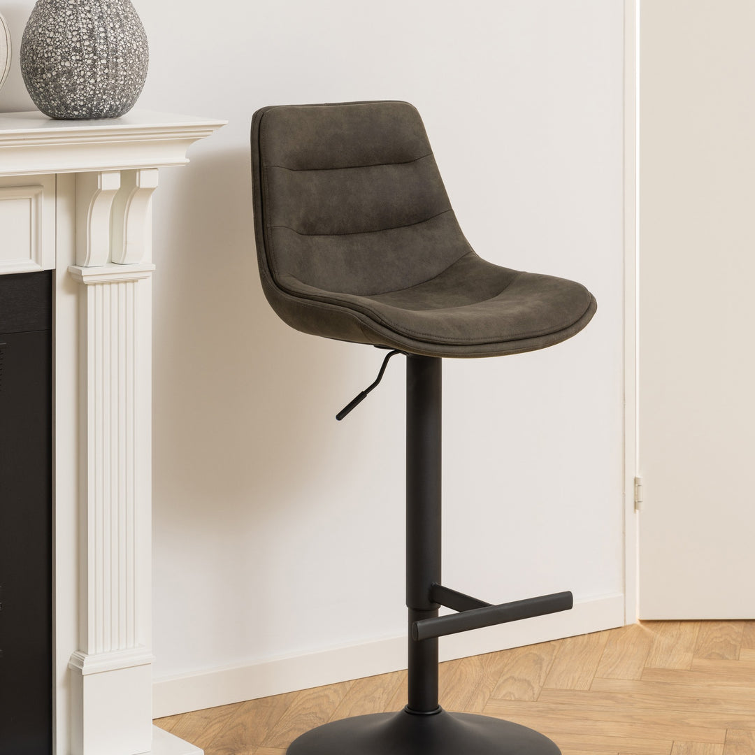 Adisa barstol i mørk grågrønn mikrofiber med sort fot, ved hvit peishylle