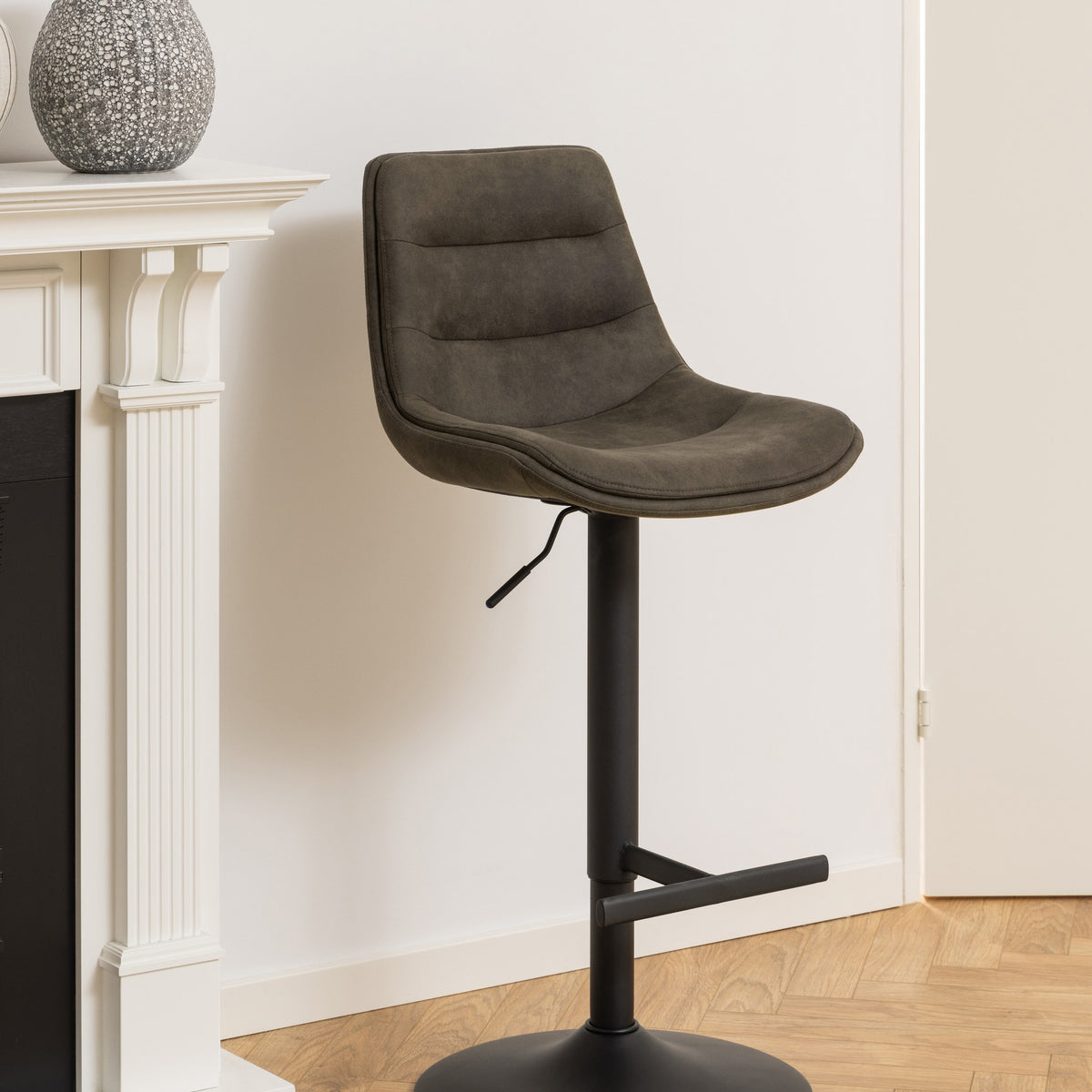 Adisa barstol i mørk grågrønn mikrofiber med sort fot, ved hvit peishylle