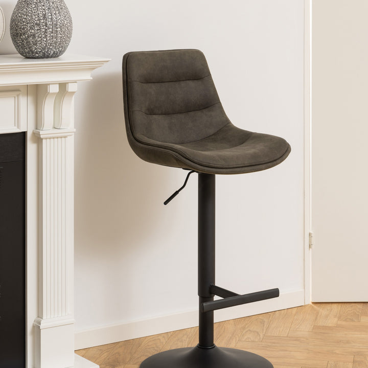 Adisa barstol i mørk grågrønn mikrofiber med sort fot, ved hvit peishylle