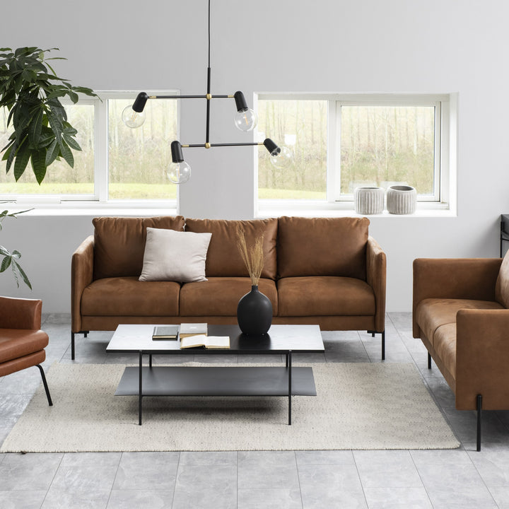 Angus sofabord med lys marmortopp og sort hylle, foran cognacfarget skinnsofa i lyst rom