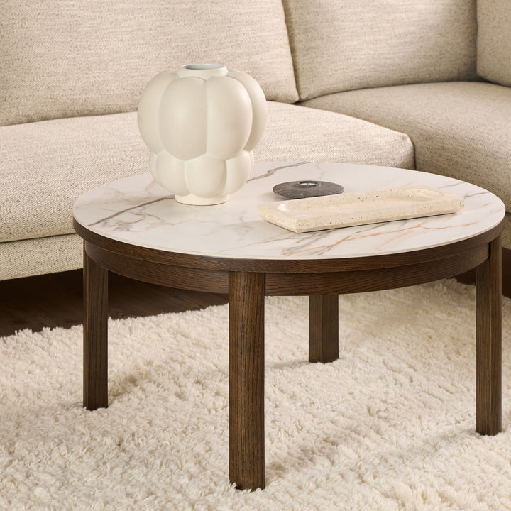 Hampton sofabord rundt i mørk eik med hvit marmorplate, i stue med beige sofa og vase.