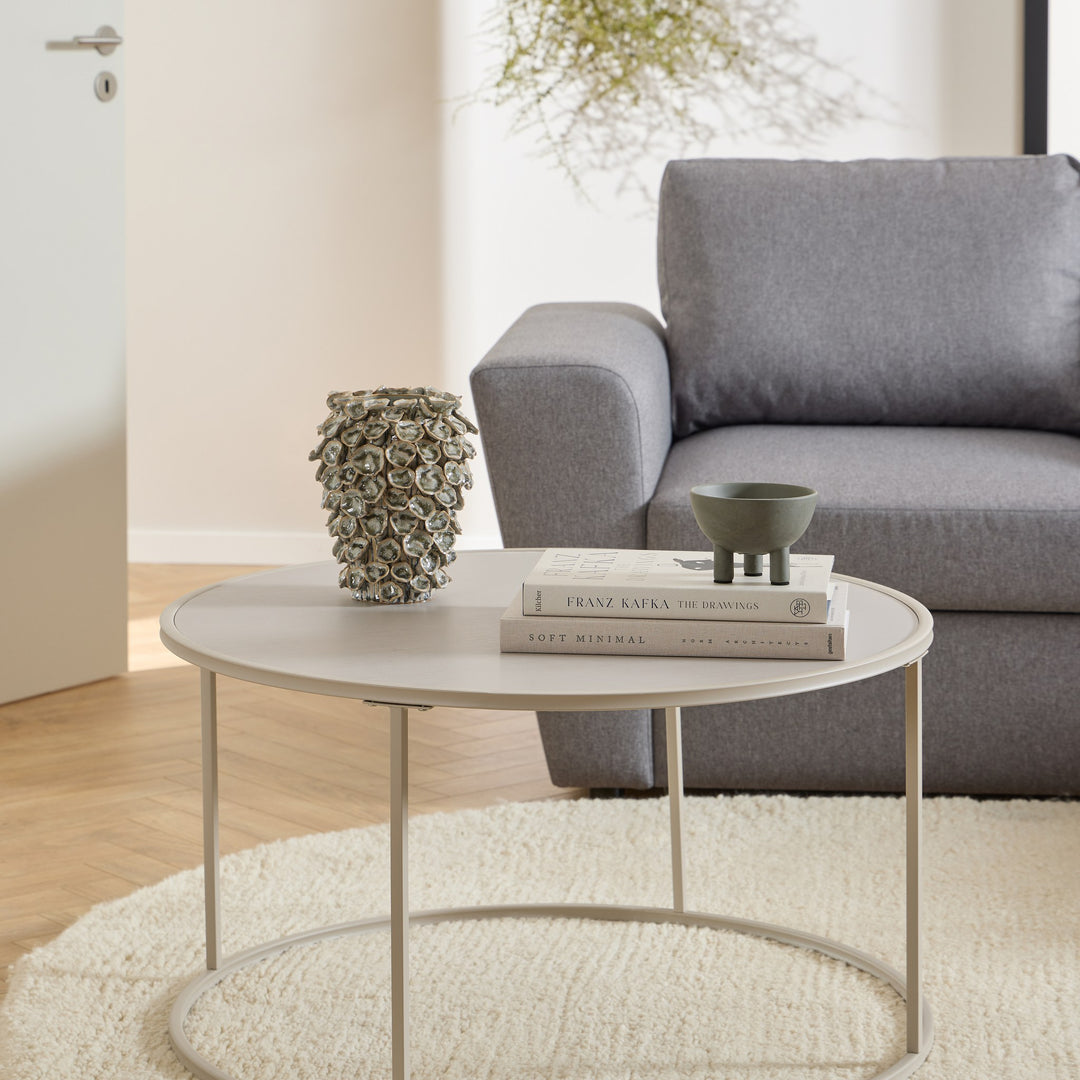 Seaford sofabord i sandfarget metall foran grå sofa, med bøker og vase