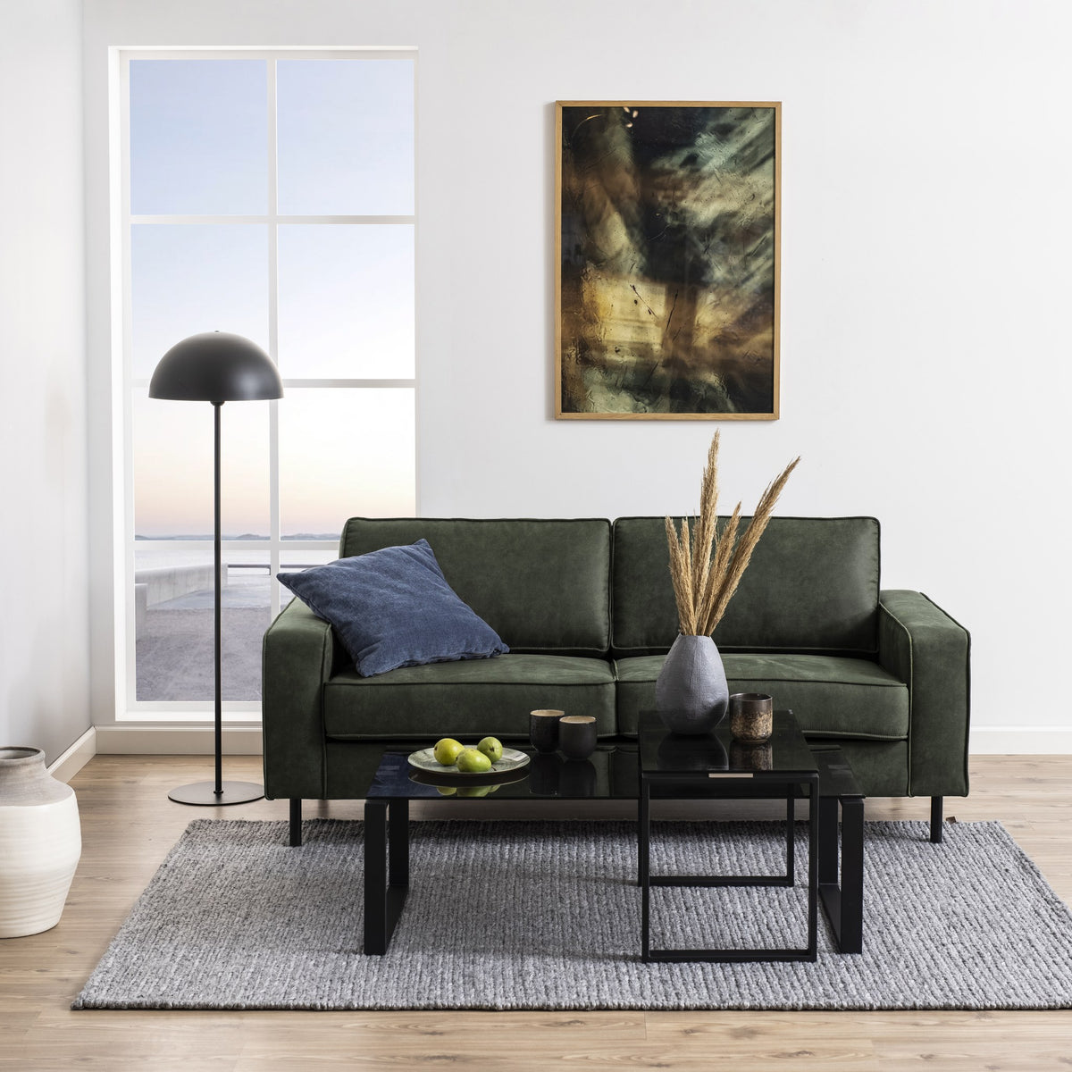 Katrine sofabord med røykfarget glass og sorte ben foran mørk grønn sofa