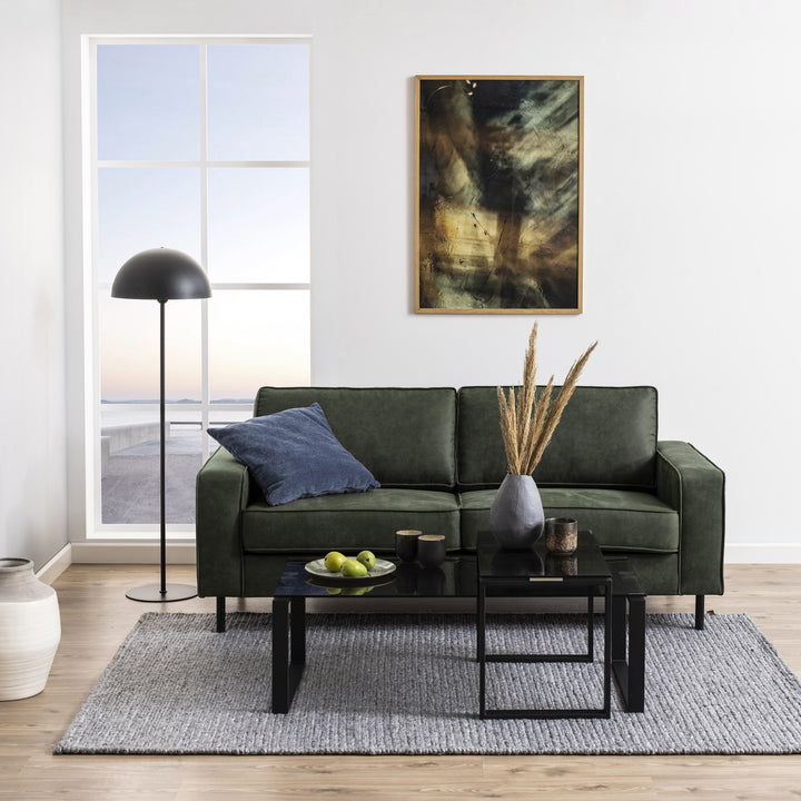 Katrine sofabord med røykfarget glass og sorte ben foran mørk grønn sofa