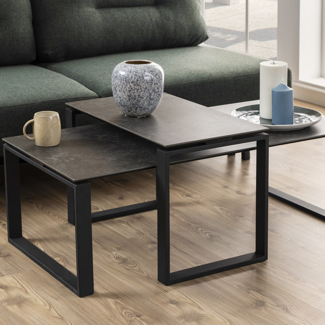 Katrine sofabord med grå keramikkplate og sort ramme foran grønn sofa, med vase og lys