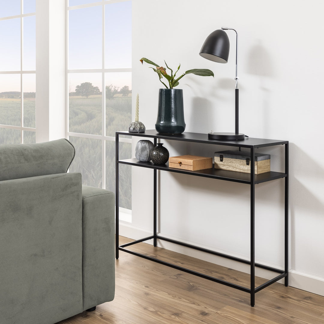 Newcastle konsollbord i sort metall med to hyller, dekorert med lampe, vase og esker