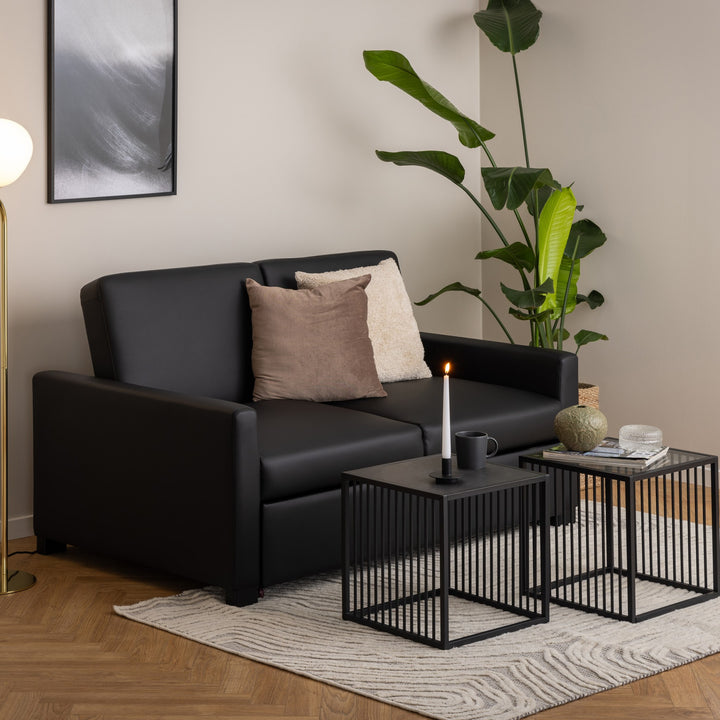 Strington hjørnebord, to sorte settbord ved sort sofa med lys, kopp, vase og bøker