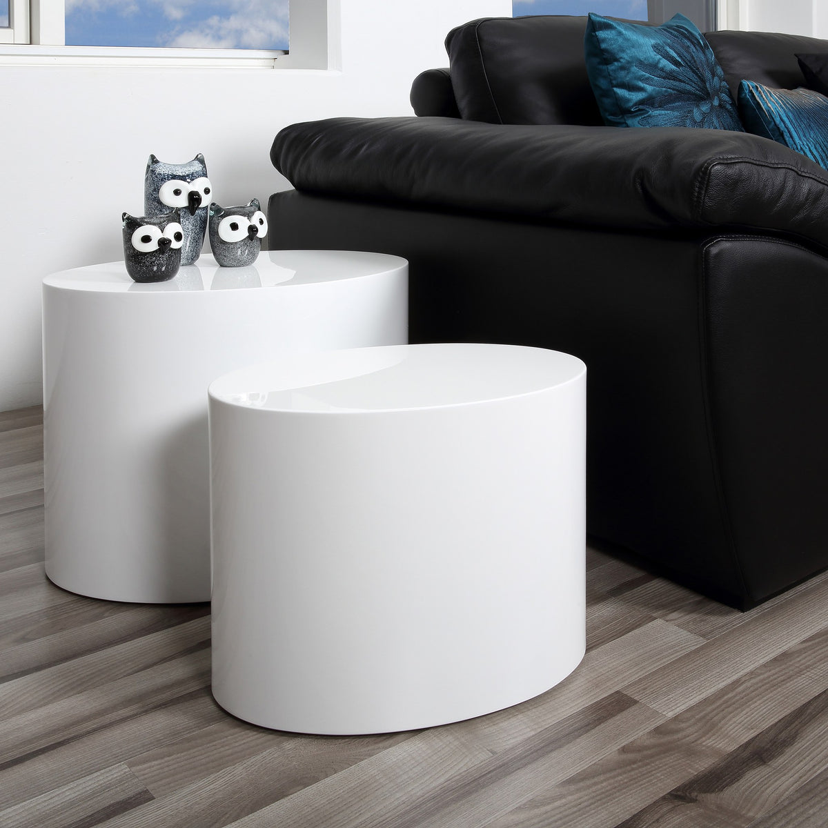Mice sidebord som ovale søyler i hvit høyglans, to bord ved sort skinnsofa med uglefigurer.